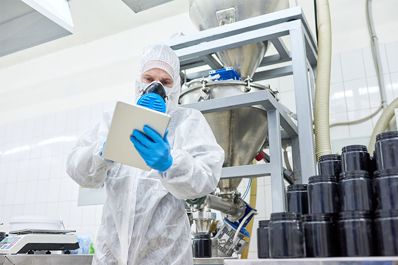 Sports nutrition production employee standing in protective clothing and using tablet computer.