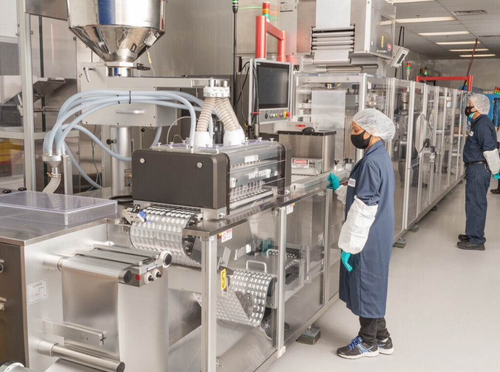 Technician operating a blister packaging machine in a cleanroom environment. Technician operating a blister packaging machine in a cleanroom environment.