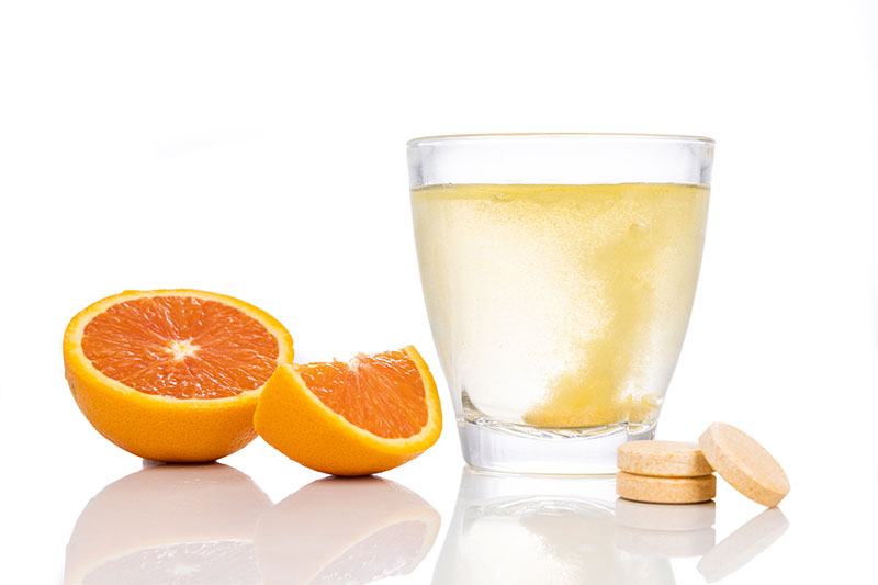 Series of orange flavored vitamin c effervescent tablet dropped and dissolve in glass of water on white background