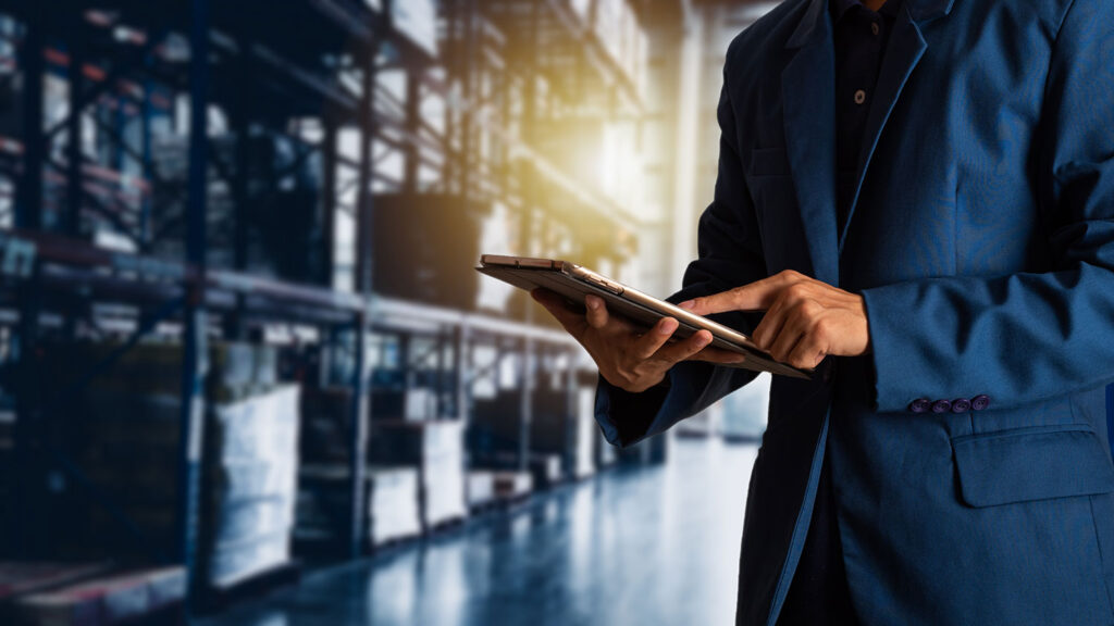 Businessman with tablet in warehouse, monitoring inventory or logistics.