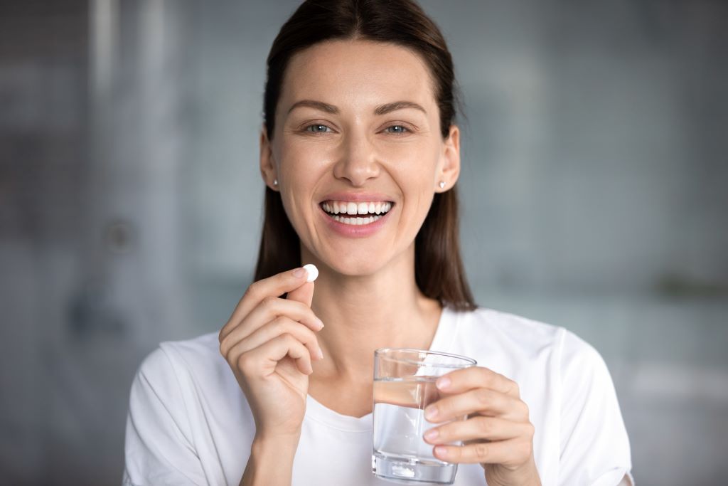 A millennial woman holding a white effervescent tablet and a glass of water in her hands.